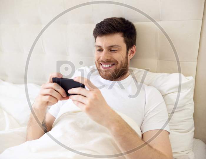 Man Laying In Bed Playing Phone Games. Man At Home Morning.