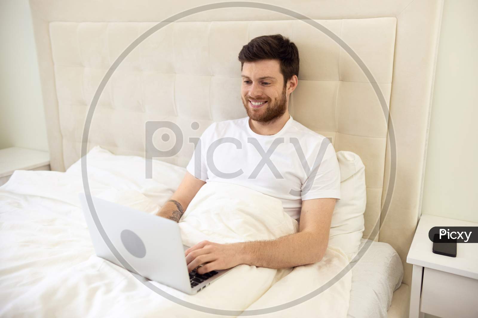 Man Working In Bed. Man Working At Home. Man Using Laptop In Bed. Quarantine, Home Work, Medical Care.