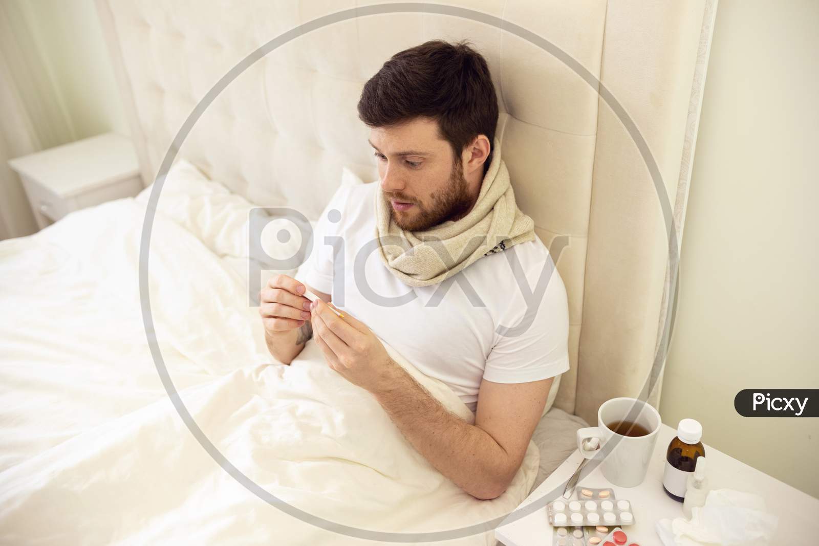 Man Sick In Bed Checking Temperature. Man Having High Temperature Watching Thermometer. Man Ill At Home.