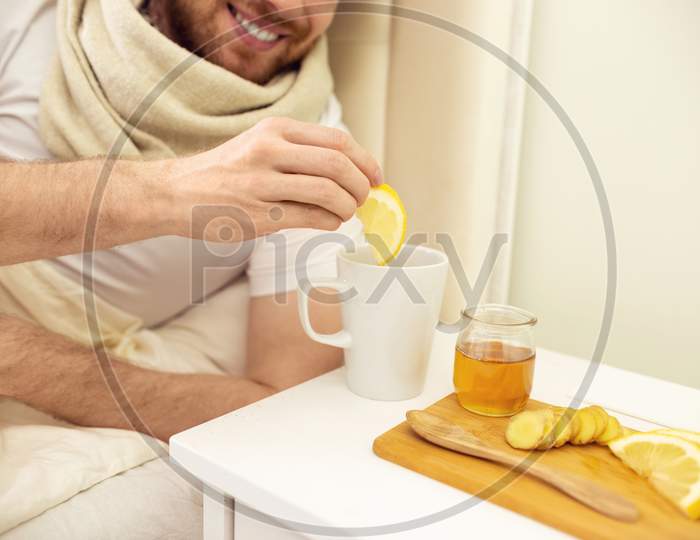 Sick Man In Bed Adding Lemon Into Tee Smilling. Man Ill In Bed Self Healing. Self Treatment At Home. Man Drinking Hot Tea In Bed. Close Up