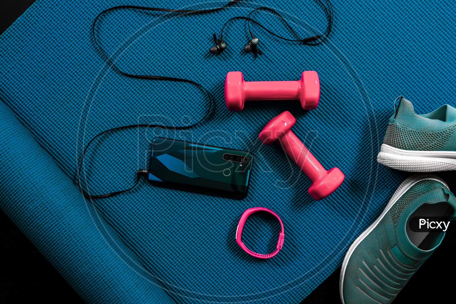 Gym flat lay with dumbbells, shoes, activity tracker, smart phone, ear phones and yoga mat. Fitness concept background with copy space