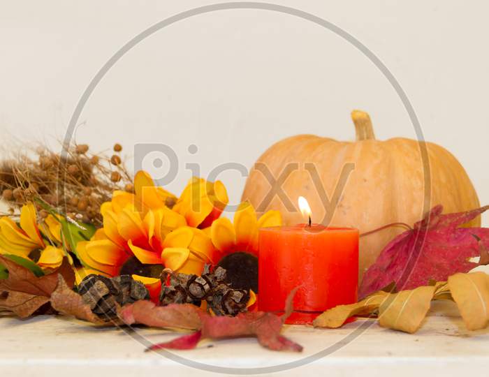 Pumpkin And Lit Candle With Autumn Harvest On White Background
