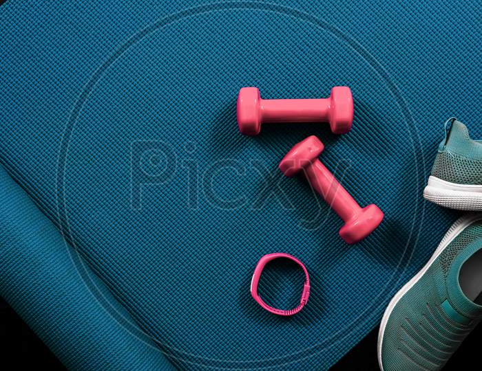 Fitness flat lay with dumbbells, shoes, activity tracker and yoga mat. Textured blue background with copy space