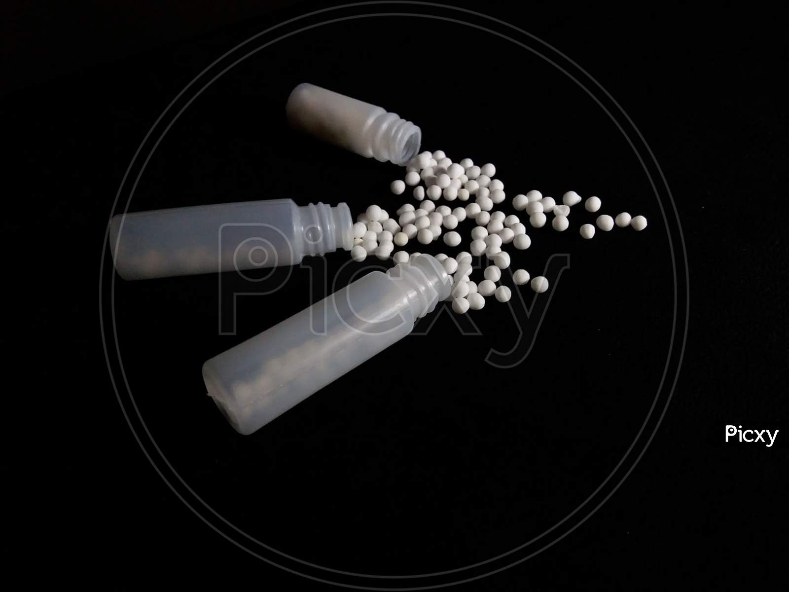 Globules/pills of homeopathy medicine scattered on black background
