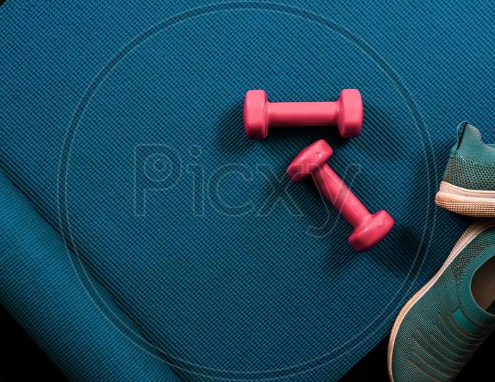 Fitness flat lay with dumbbells, shoes and yoga mat. Blue gym background template with copy space