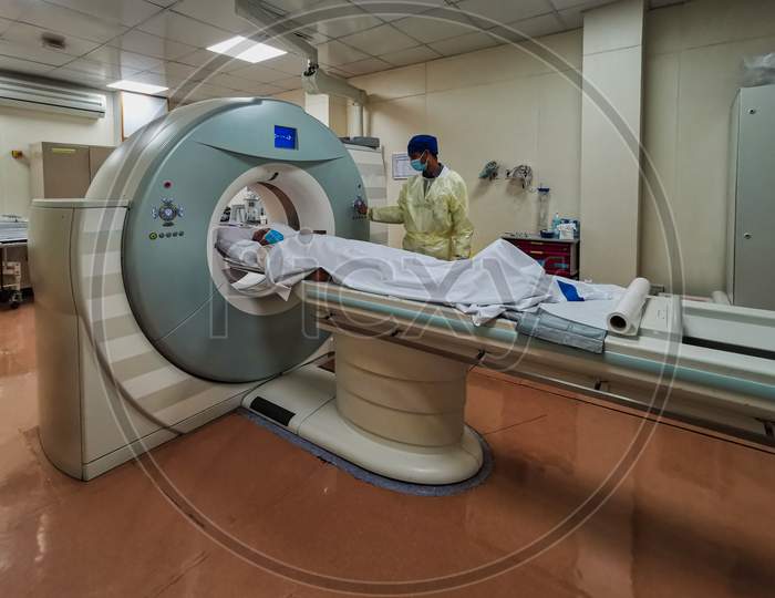 Computed Tomography machine (CT) in Radiology Department with radiology technician wearing personal protective equipment (PPE) preparing COVID-19 patient for examination