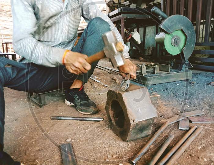 Worker Beating Or Hit A Iron Piece To Give A Shape In Iron Workshop With Hammer