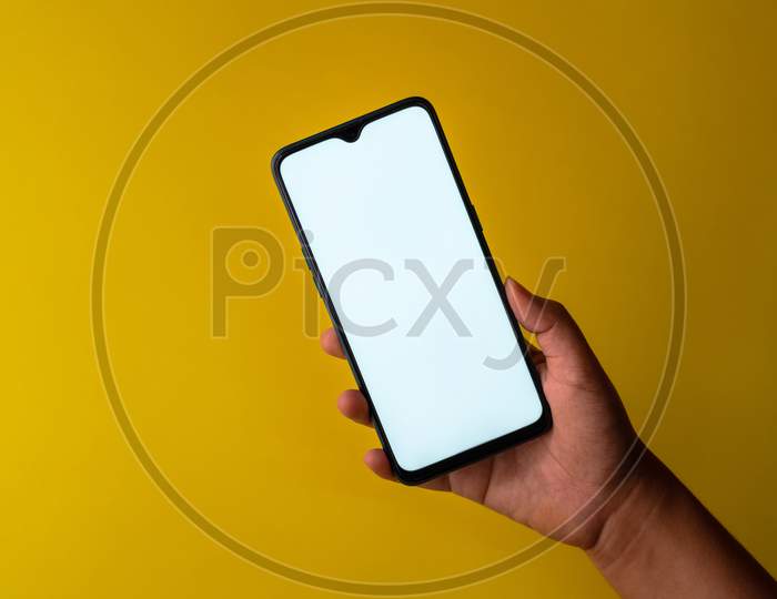 Smart phone with white screen held against a plain yellow background with copy space