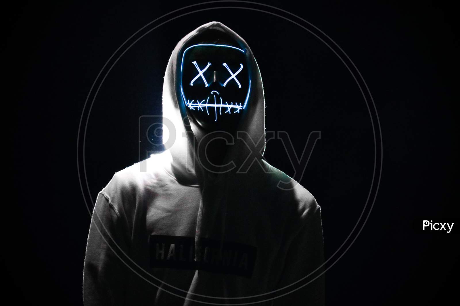 A Man Wearing A Gray Hoodie With lighting White Glowing Mask In The Dark Background. Halloween And Horror Concept.