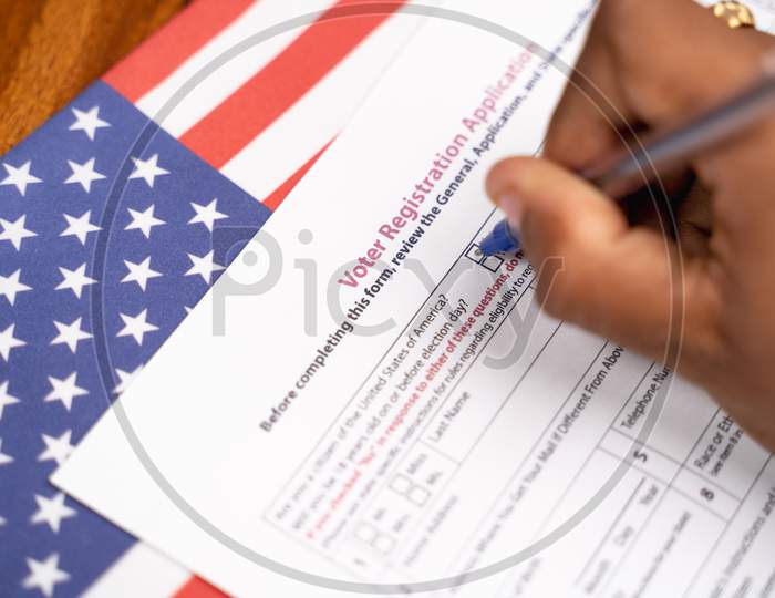 Maski, India - 23, June 2020 : Close Up Of Hands Filling President Voter Registration Application With Us Flag As Background For Upcoming Election.