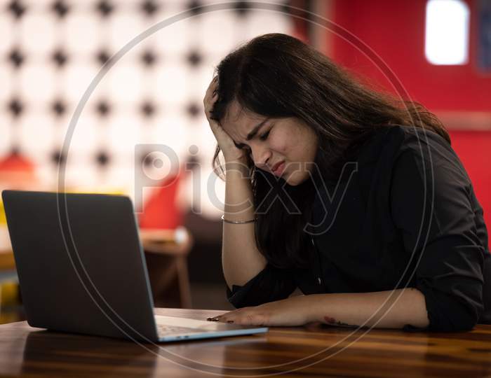Portrait of a beautiful, young and intelligent-looking Indian Asian woman student thinking wearing a shirt smiling as she works on her laptop at a workplace