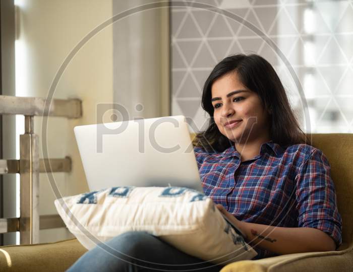 Portrait of a beautiful, young and intelligent-looking Indian Asian woman student wearing a shirt  smiling as she works on her laptop