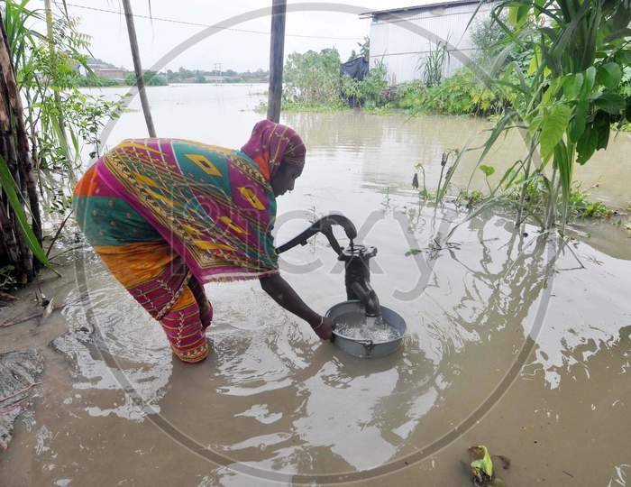 A Woman Collects Drinking Water From A Hand Pump With Her House Inundated With Flood Water In The Flood Affected Morigaon District Of Assam On June 25,2020.