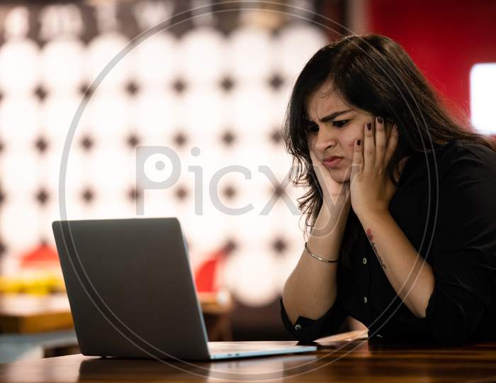 Portrait of a beautiful, young and intelligent-looking Indian Asian woman student thinking wearing a shirt smiling as she works on her laptop at a workplace