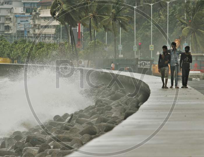 People walk on the promenade as sea waves strike at Marine Drive during rains, in Mumbai on June 18, 2020.