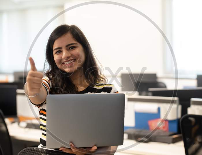smiling young woman gestures thumbs up while working on a laptop