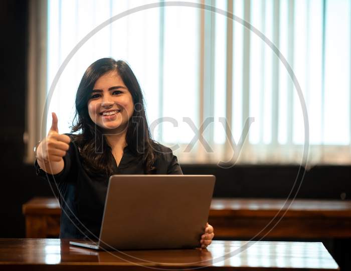 Smiling Young Indian woman showing thumbs up gesture as she works on a Laptop