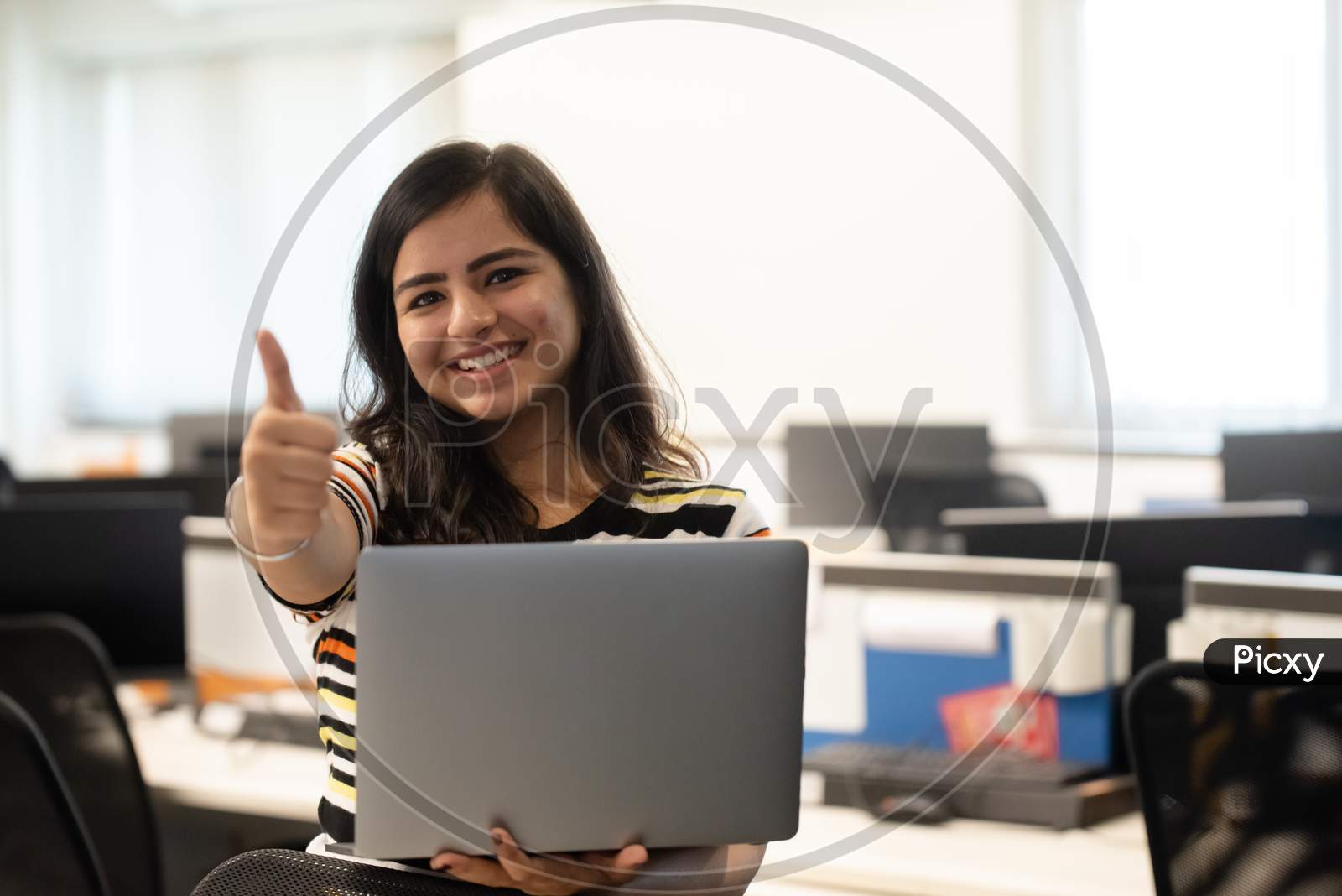 smiling young woman gestures thumbs up while working on a laptop