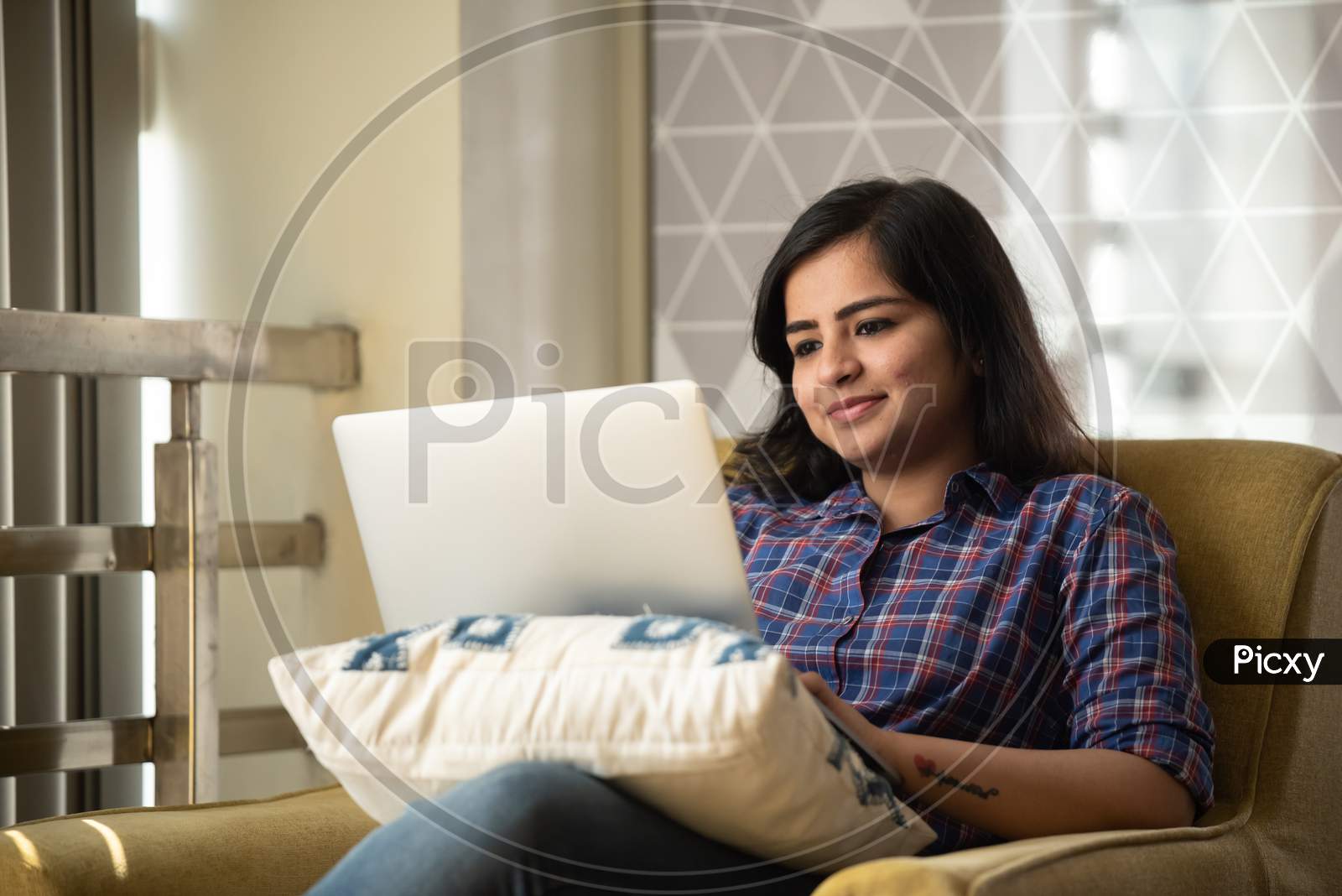 Portrait of a beautiful, young and intelligent-looking Indian Asian woman student wearing a shirt  smiling as she works on her laptop