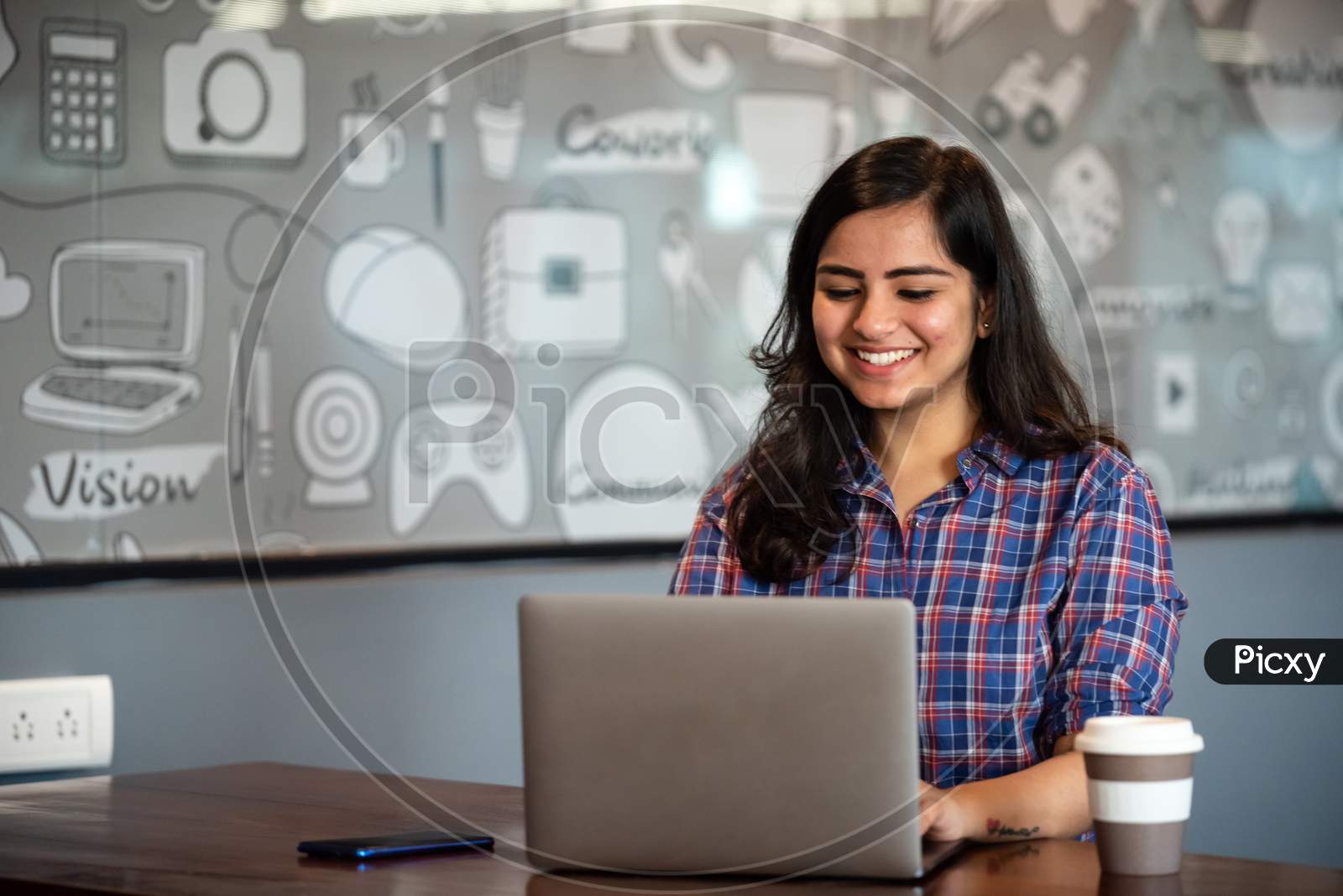 Portrait of a beautiful, young and intelligent-looking Indian Asian woman student wearing a shirt and smiling as she works on her laptop
