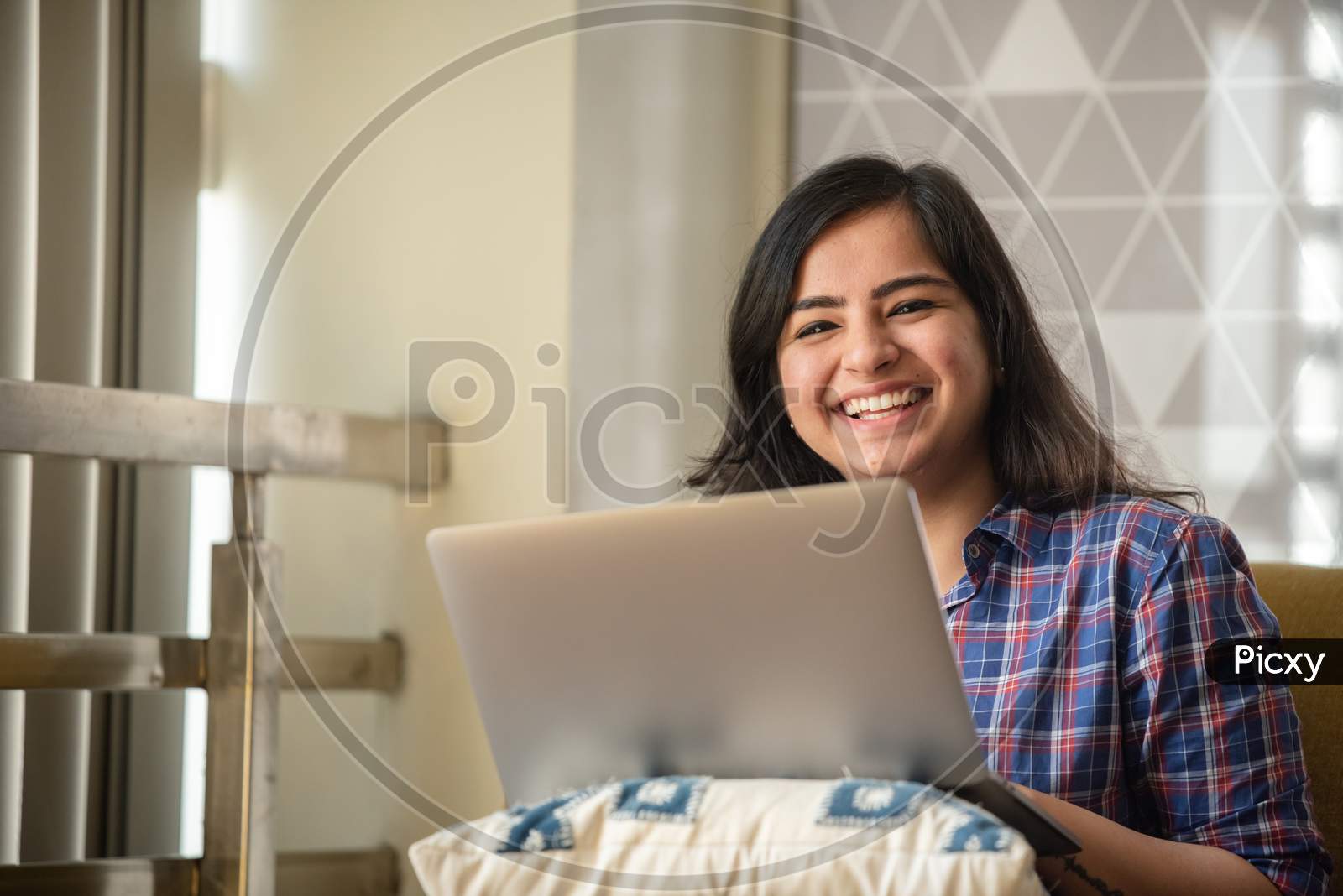 Portrait of a beautiful, young and intelligent-looking Indian Asian woman student wearing a shirt smiling as she works on her laptop