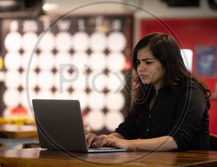 Portrait of a beautiful, young and intelligent-looking Indian Asian woman student wearing a shirt smiling as she works on her laptop at a workplace