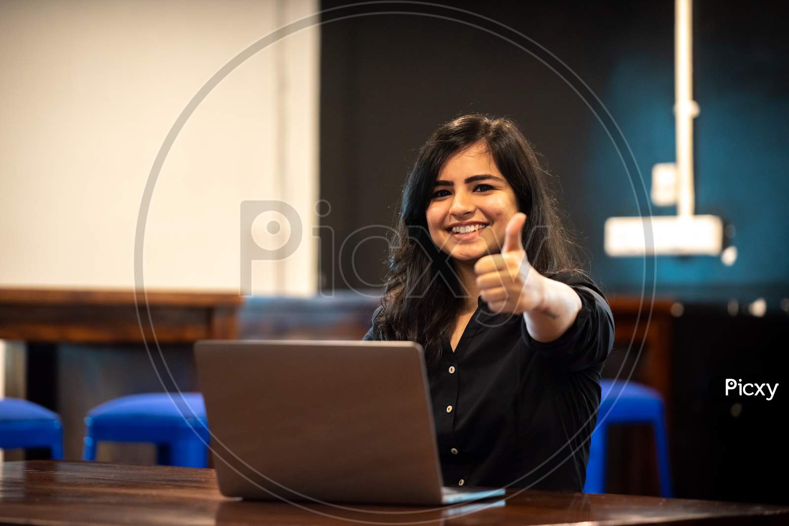 Smiling Young Indian woman showing thumbs up gesture as she works on a Laptop