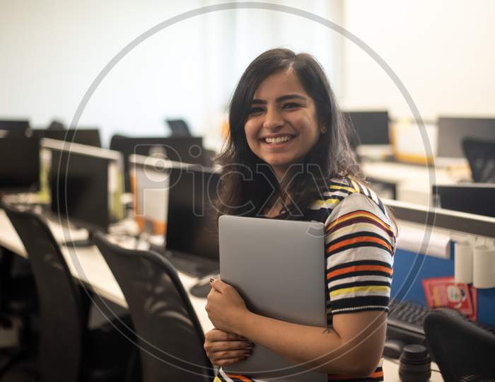 Portrait of a beautiful, young and intelligent-looking Indian Asian woman student wearing a T-shirt  smiling as she works on her laptop