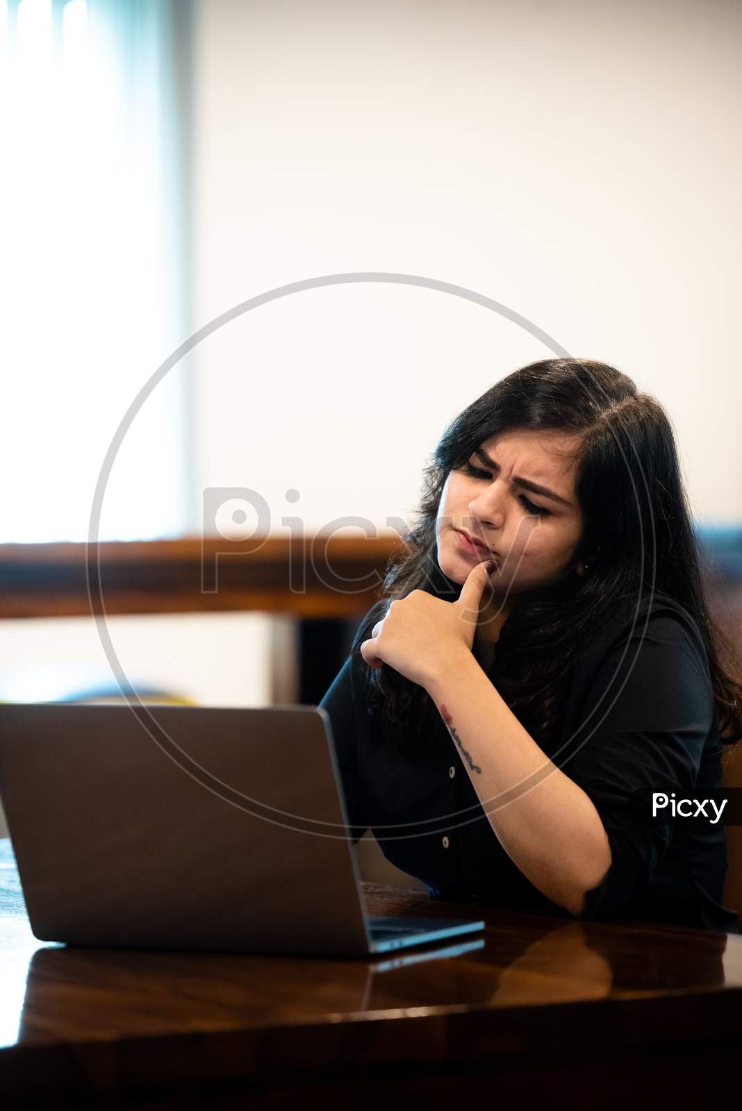 Young Indian girl thinking as she works on a laptop