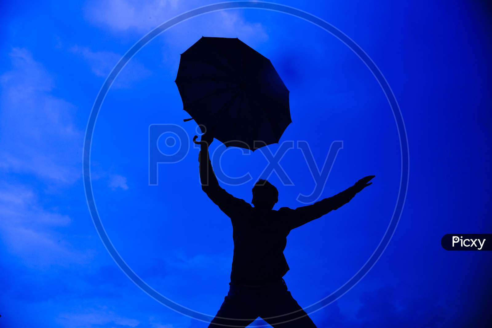 Silhouette Happy Man Flying Holding Open Umbrella Against Blue Sky