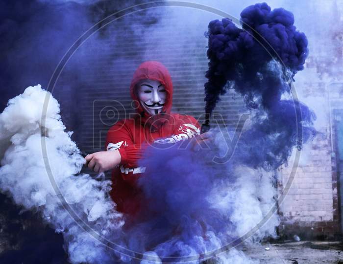Man Wearing Red Jacket And Fawkes mask  Surrounded By Purple And White Smoke.