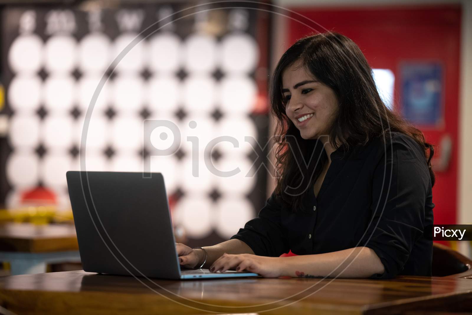 Portrait of a beautiful, young and intelligent-looking Indian Asian woman student wearing a shirt smiling as she works on her laptop at a workplace
