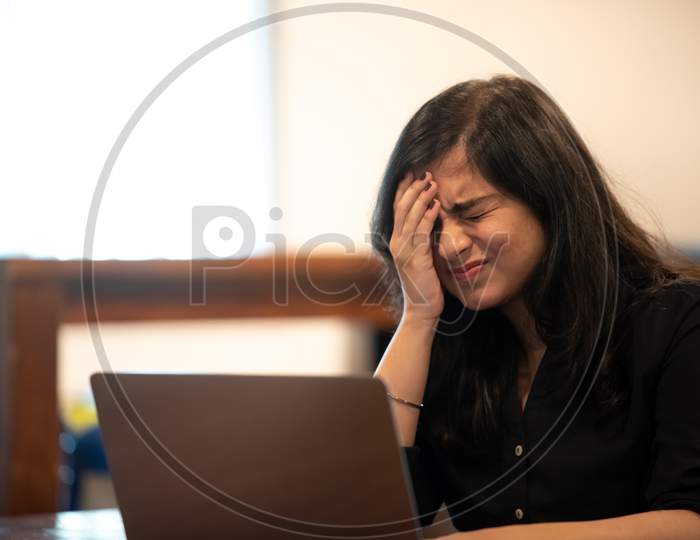 Portrait of a beautiful, young and intelligent-looking Indian Asian woman student wearing a shirt feeling distressed as she works on her laptop at a workplace