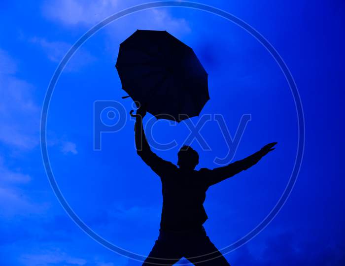 Silhouette Happy Man Flying Holding Open Umbrella Against Blue Sky