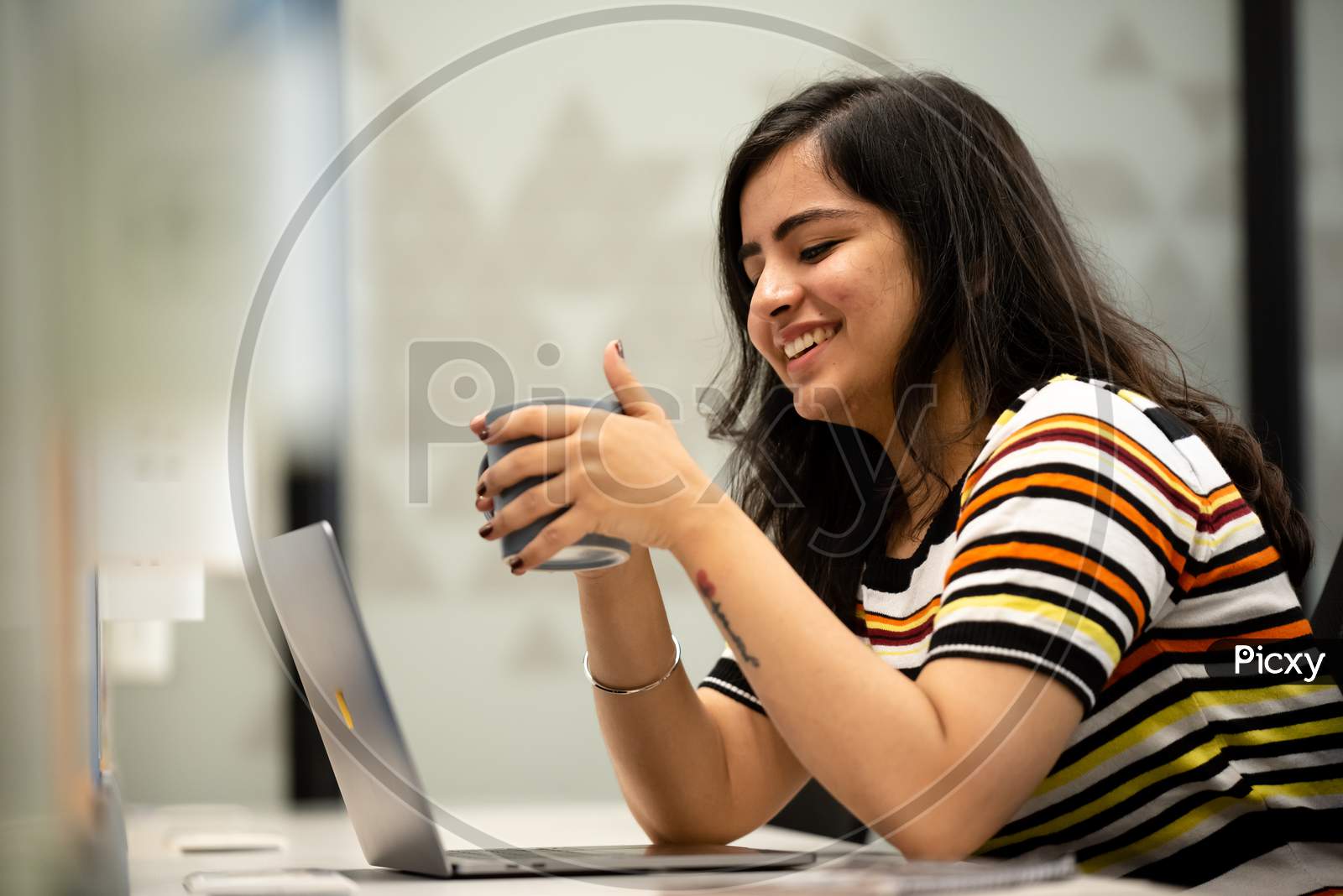 smiling young woman drinks coffee at work