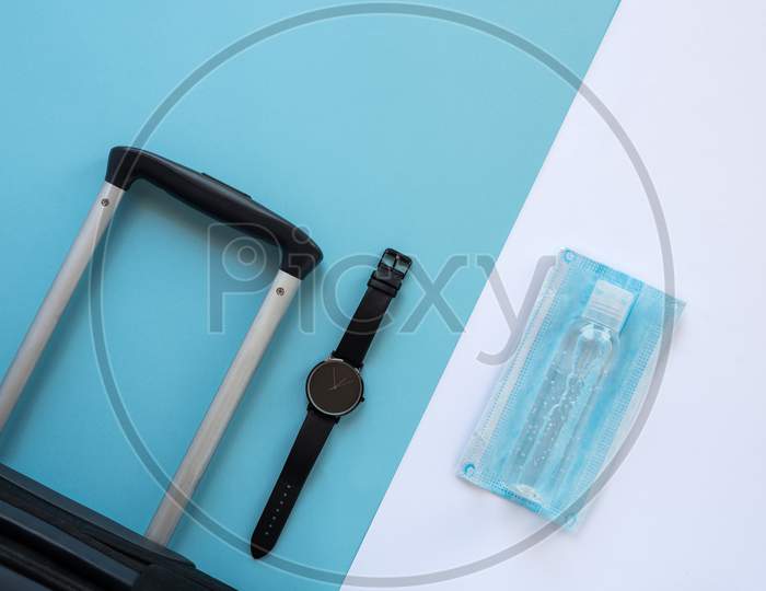 Accessories Of A Traveller On The Summer Holidays 2020 With The Coronavirus. Black Suitcase, Face Mask, Hydroalcoholic Gel And Clock