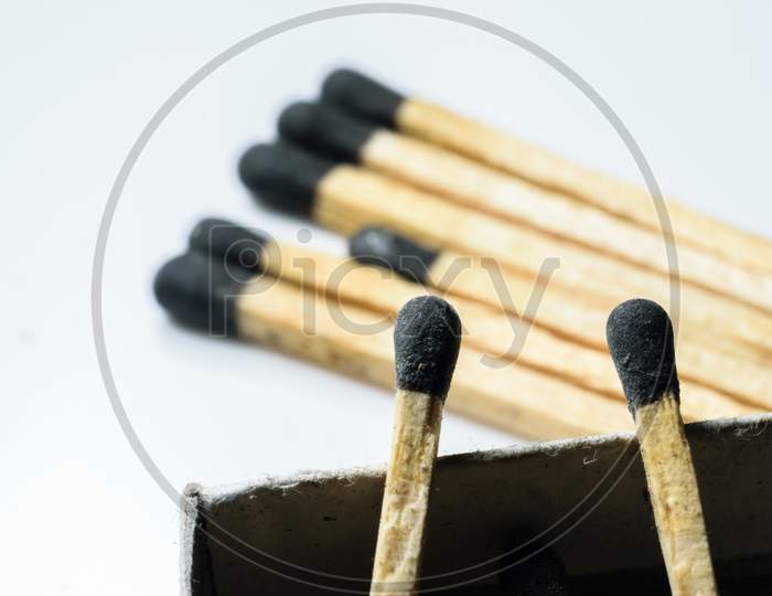 Two Match Sticks In Focus Over The Edge Of A Match Box And Multiple Match Sticks Laying On The Floor In The Background. White Background
