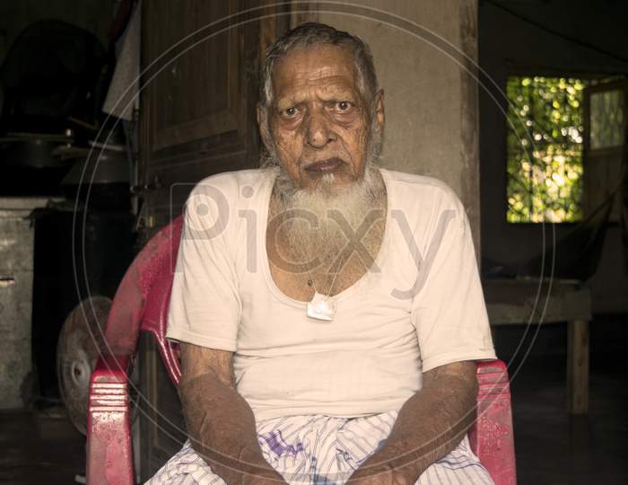 An old Indian bearded person sitting on chair
