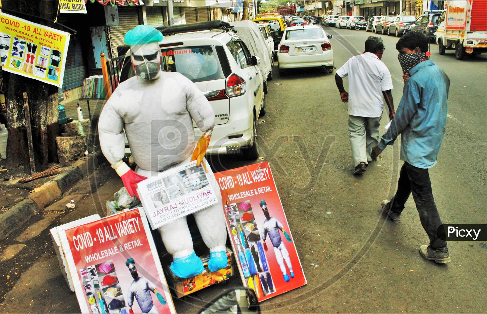 People walk past a PPE kit makeshift mannequin displayed by a shopkeeper by the roadside, in Mumbai, India on June 20, 2020.