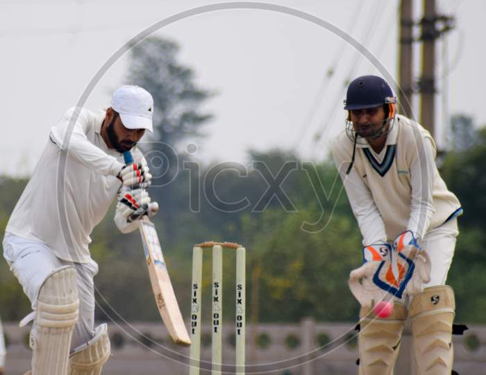 New Delhi India – March 3 2020 : Full length of cricketer playing on field during sunny day in local playground, Cricketer on the field in action, Players playing cricket match at field