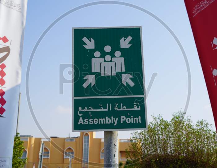 Dubai Uae - November 2019: Emergency Assembly Point Information Sign In White Paint On Green Background Fixed To A Pole To Direct People Where To Go In Case Of An Emergency.
