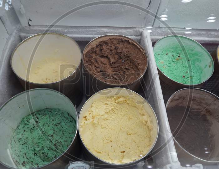Bulk Ice Cream Kept In Large Round Containers Behind Glass At Gelato Shop. Ice Cream In A Candy Store. Pistachio, Chocolate, Strawberry, Banana Ice Cream Bar At All You Can Eat Buffet Restaurant.