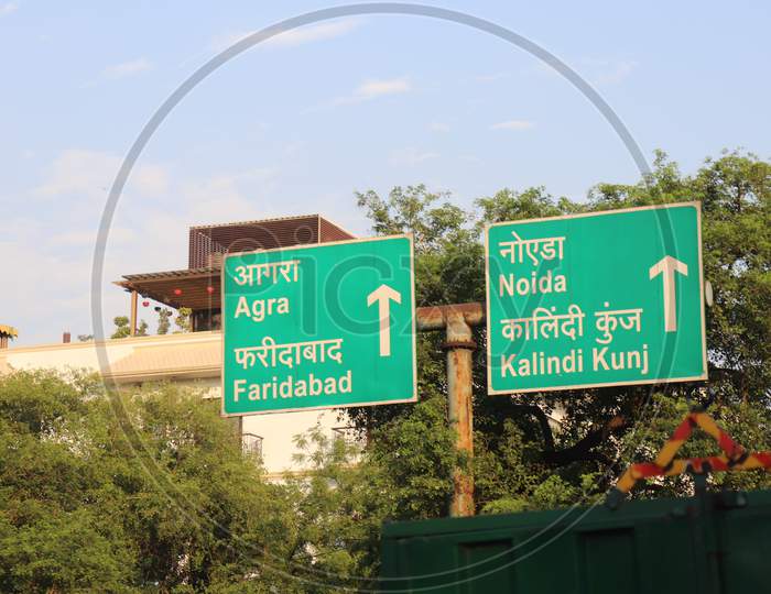 "New Delhi/India -21.06.2020: Sign Board In Green Showing Distance Of Agra , Noida , faridabad and kalindi kunj Texture White  English Language Green Board Near tree "
