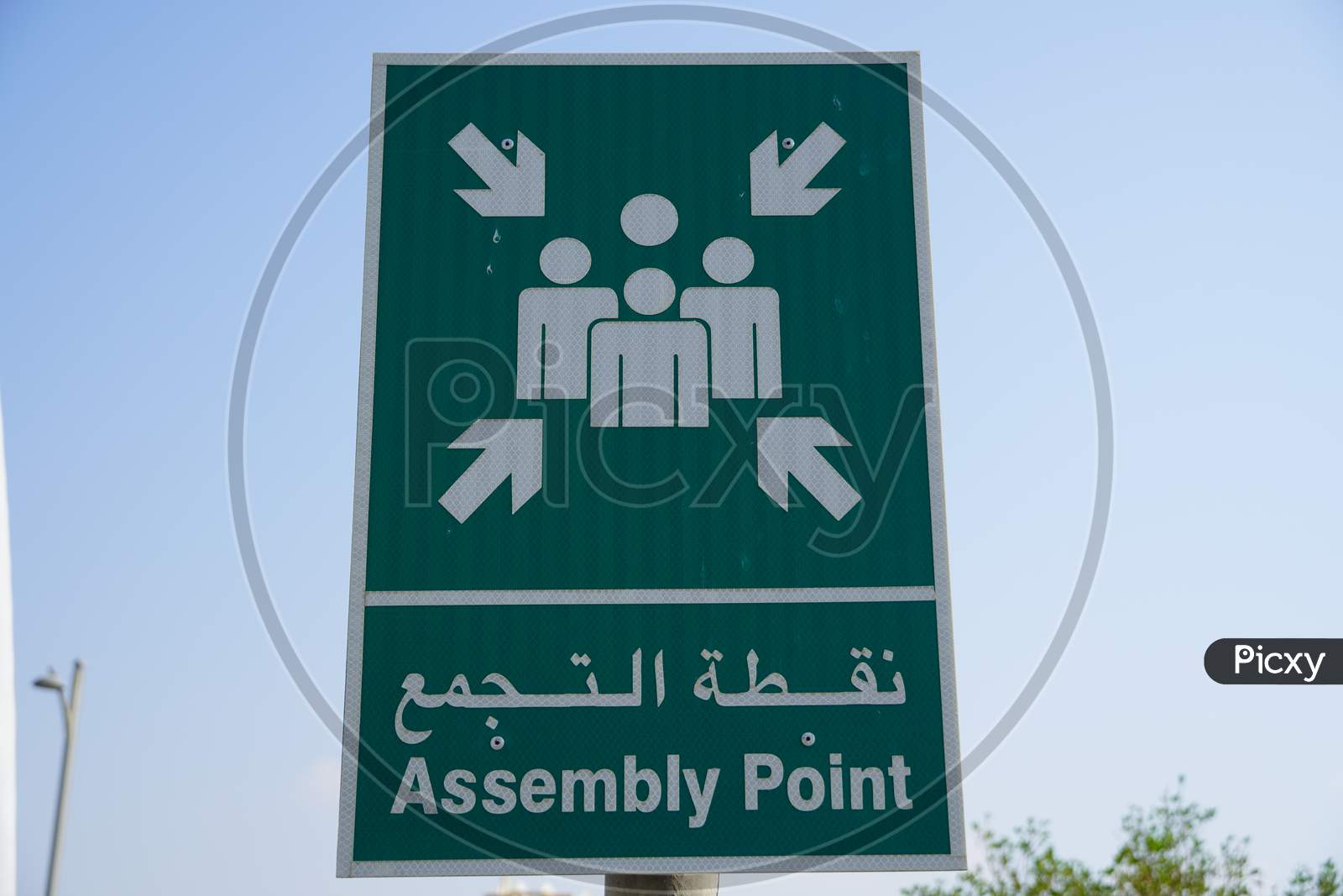 Emergency Assembly Point Information Sign In White Paint On Green Background Fixed To A Pole To Direct People Where To Go In Case Of An Emergency.
