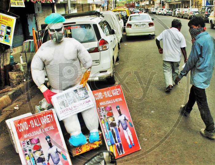 People walk past a PPE kit makeshift mannequin displayed by a shopkeeper by the roadside, in Mumbai, India on June 20, 2020.