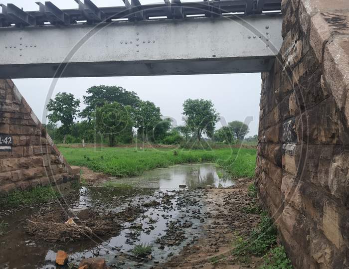 Old Railway Bridge In India With Green Grass And Stream Under In It