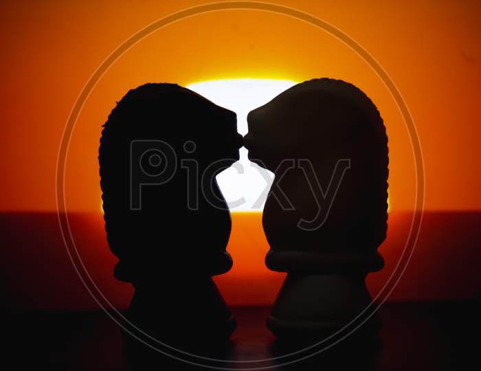 Silhouette Chess Pieces Knights Kissing Each Isolated On Sunrise Background. Confrontation Of Chess Pieces.Chess Pieces Knights Head.