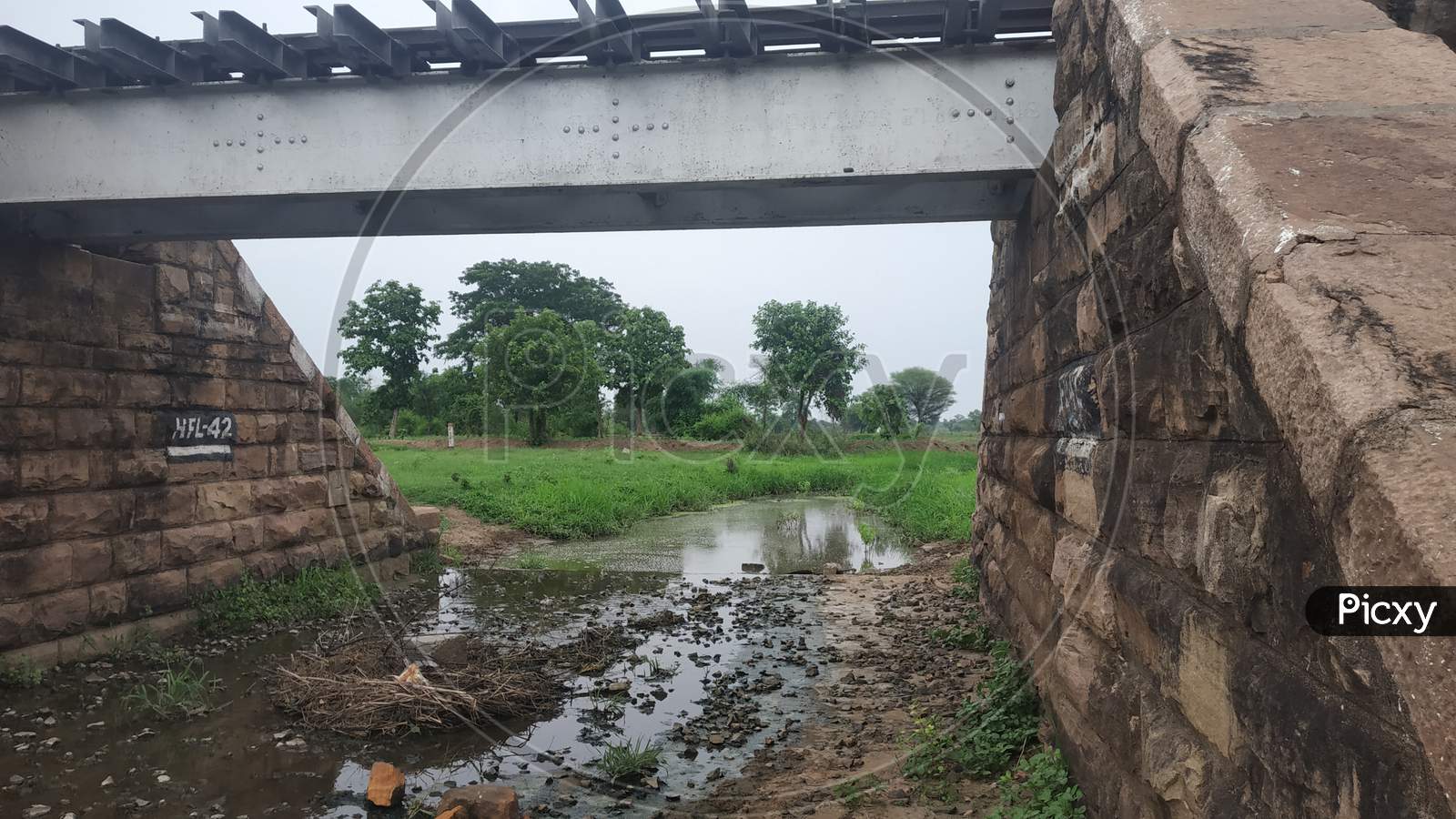 Old Railway Bridge In India With Green Grass And Stream Under In It