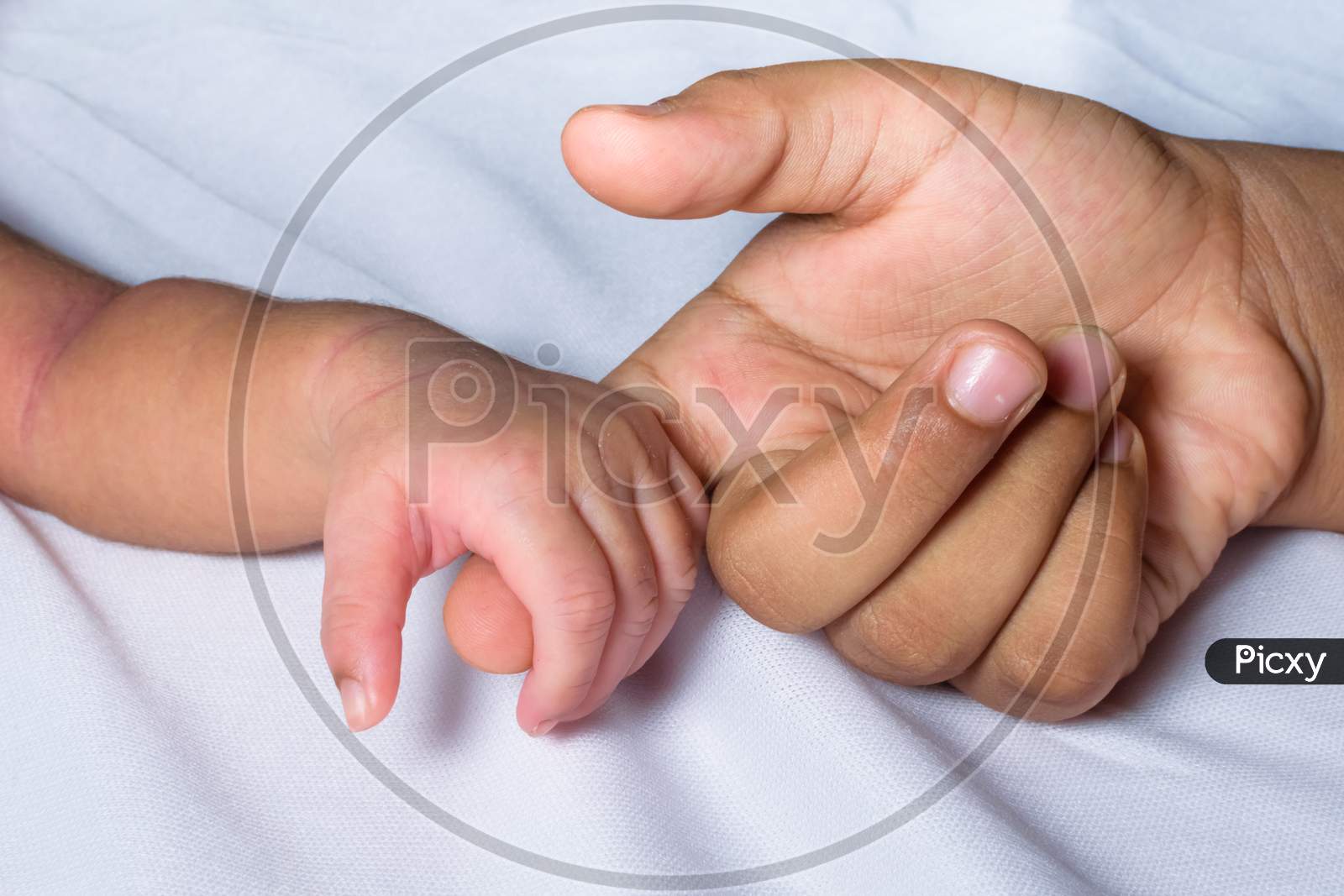 Index Finger Of A Young Boy Held By A Newborn Baby In A White Background
