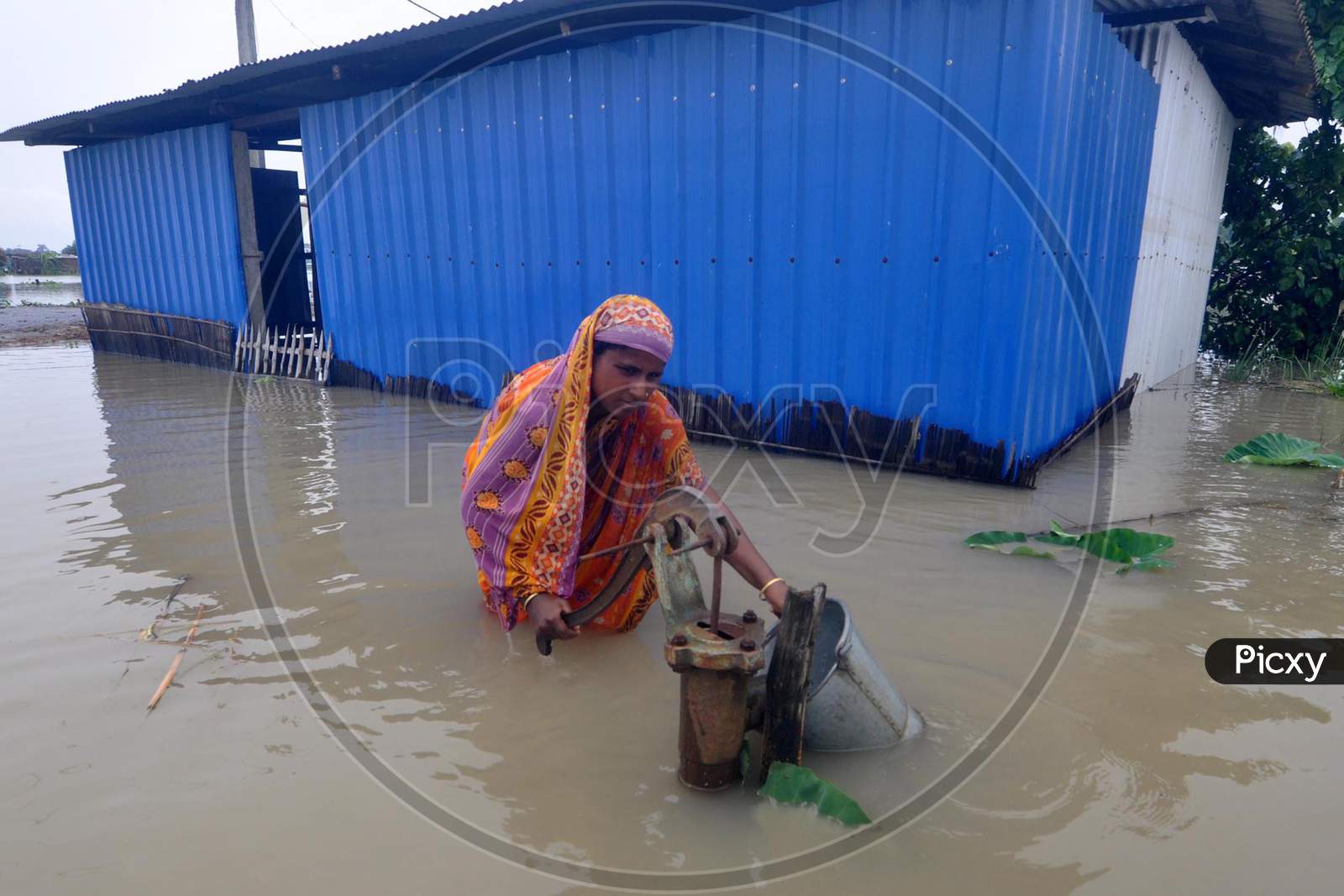 A woman fetches water from a partially submerged hand pump in a flood-affected village in Morigaon  district in the northeastern state of Assam on june 28,2020.